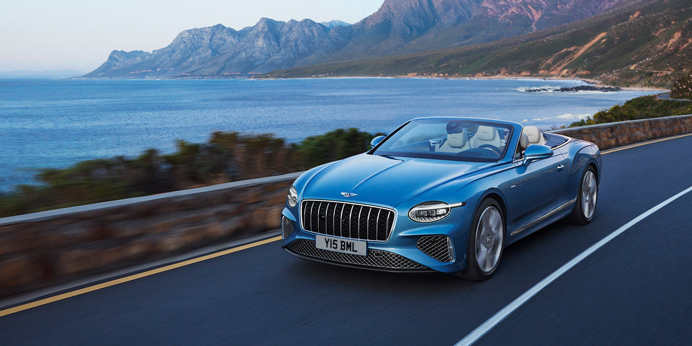 Bentley Knokke New Bentley Continental GTC Azure convertible in Light Windsor blue paint with 22 inch Azure wheels and chrome grill, driving dynamically by the sea