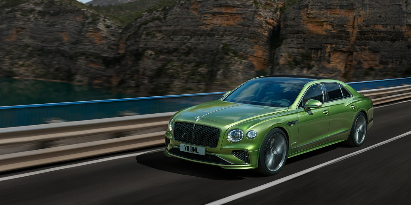 Bentley Knokke Bentley New Flying Spur Speed v8 hybrid sedan driving dynamically on a mountain road in Tourmaline Green paint