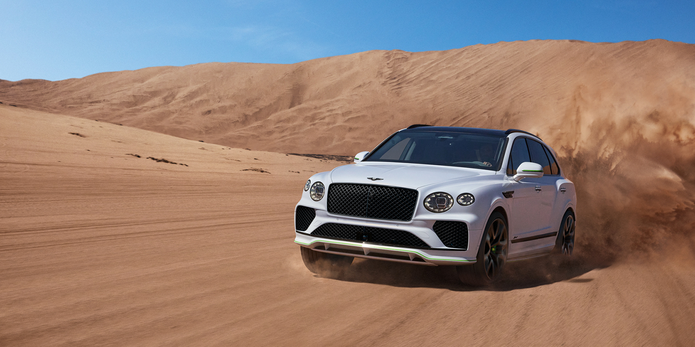 Bentley Knokke Bentley Bentayga Speed SUV front three quarter in Snow Quarts Pearlescent by Mulliner white paint driving dynamically through the desert