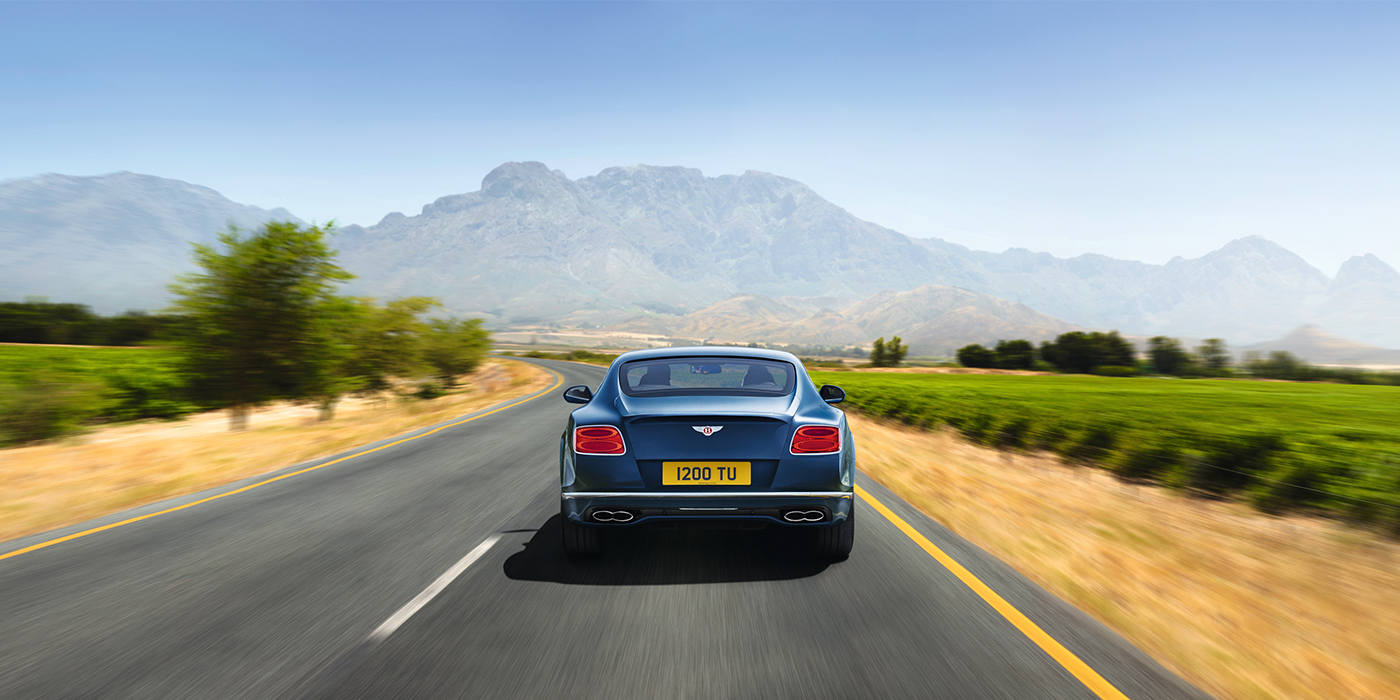 Bentley Knokke Bentley Pre Owned Bentley Continental GT in Marlin blue paint seen from rear on country road