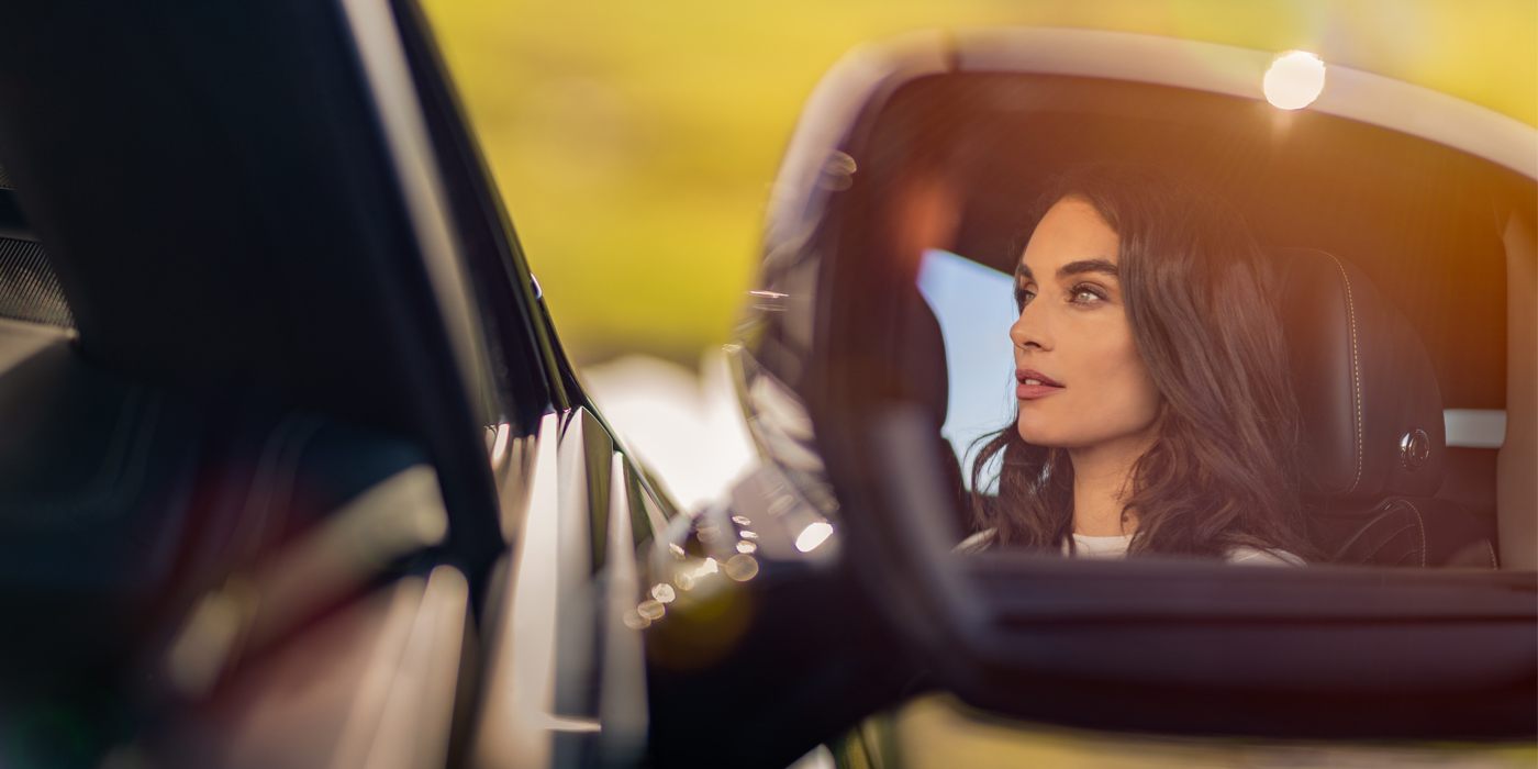Bentley Knokke profile of dark haired woman's face in mirror of Bentley car in sunlight