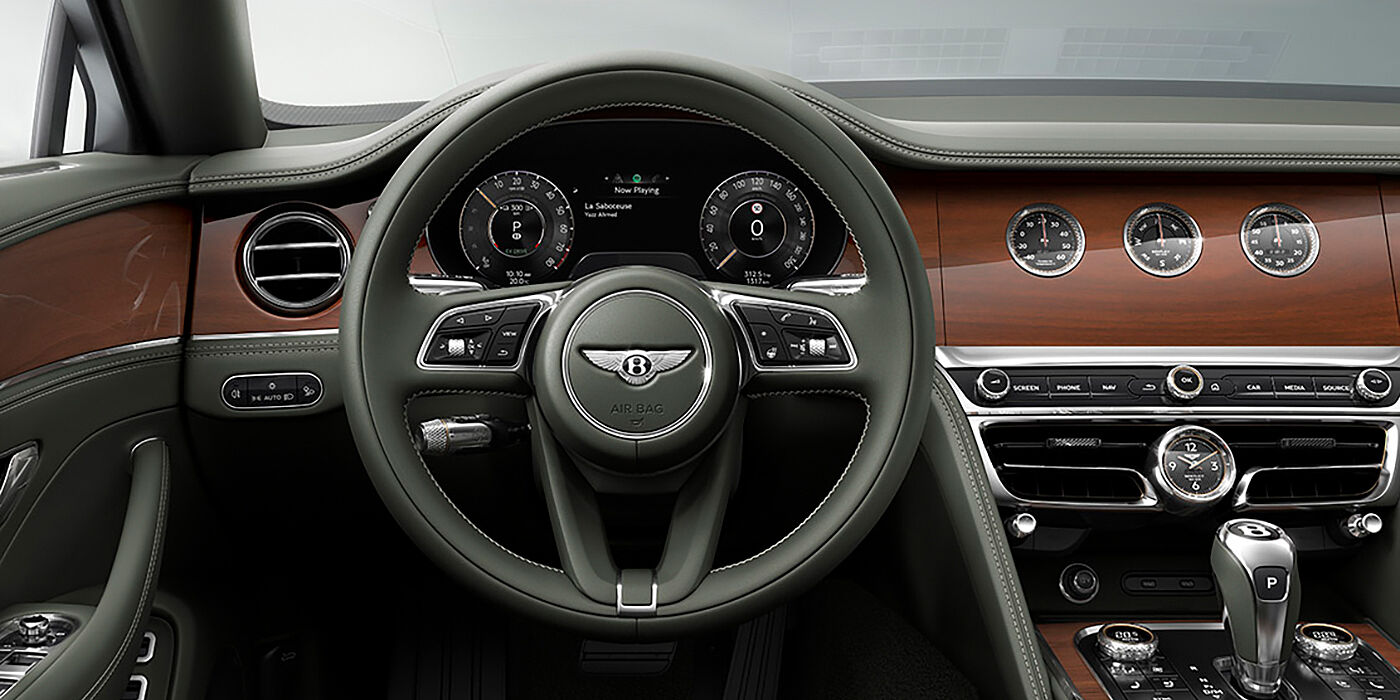 Bentley Knokke New Bentley Flying Spur sedan front cabin in Cumbrian Green hide and Crown Cut walnut veneer showing steering wheel and Rotating Display with three clocks on face
