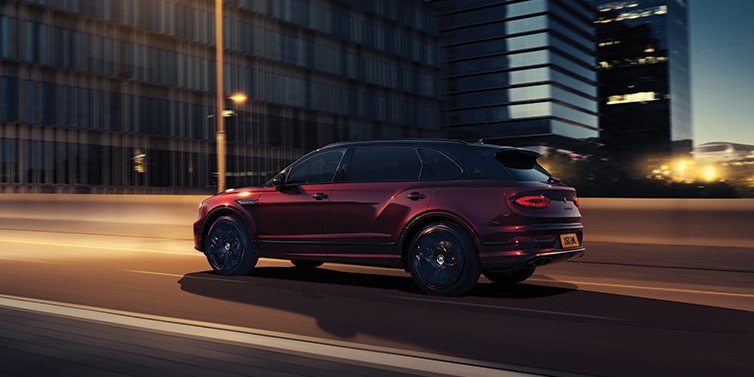 Bentley Knokke Bentley Bentayga Extended Wheelbase Mulliner SUV in Cricket Ball red paint driving dynamically in city at night